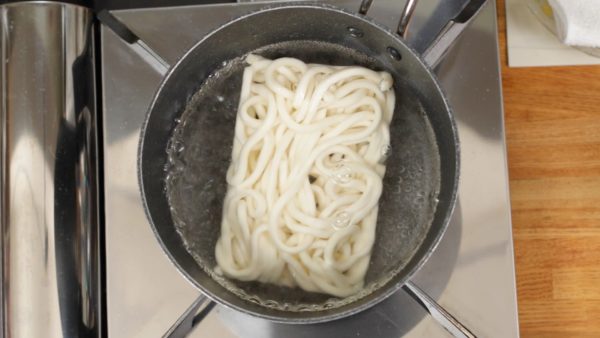 Let's make the curry udon. Place the frozen udon noodles into a pot of boiling water. Loosen up the noodles. Then, boil for 30 seconds.
