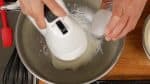 Mache nun das Baiser. Schlage die gekühlten Eiweiß mit einem Handrührgerät auf. Lass den Zucker in drei Portionen hinzurieseln, schlage die Eiweiß insgesamt für eineinhalb bis zwei Minuten auf.