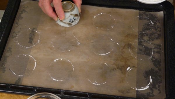 Next, dust the edge of a 5cm (2") diameter cup with any type of flour or starch. Then, as a rough guide, make 12 circles where the choux batter will be placed on the parchment paper.