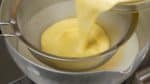 然後，用一個濾網去把蛋黃過濾到鍋裡的牛奶裡。打開煤氣爐。繼續混合卡士達醬直到它變稠。