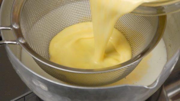 Then, using a mesh strainer, strain the egg yolk into the pot of the milk. Turn on the burner. Continue mixing the pastry cream until it thickens.