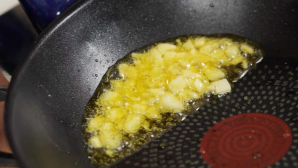 Add the olive oil to a pan. Put in the coarsely chopped garlic clove. Turn on the burner and saute it on low heat. You can tilt the pan to submerge the garlic in the oil. When the garlic is golden brown, remove and set it aside.