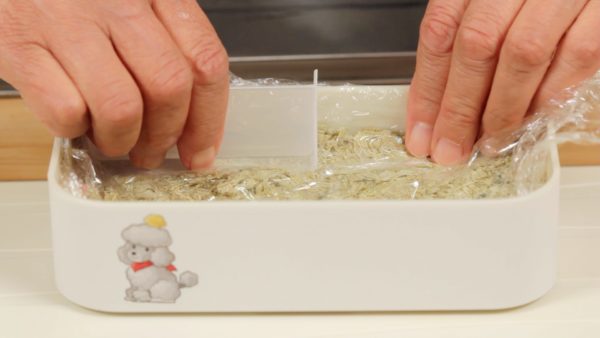 Cover with a plastic wrap. And thoroughly press the rice using a divider attached with the bento box.