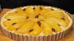 Arrangez la compote de pomme en cercle sur la crème. Les pommes devraient légèrement se superposer. Coupez le reste des pommes en deux et remplissez le milieu de la tarte avec. Répartissez les raisins secs dessus. Pressez doucement les pommes pour uniformiser la surface. 