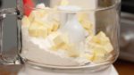 Prepariamo l'impasto per la crostata. Versate in un robot da cucina la farina fatta raffreddare. Aggiungete il burro tagliato a cubetti da 1 cm. Livellate delicatamente gli ingredienti.