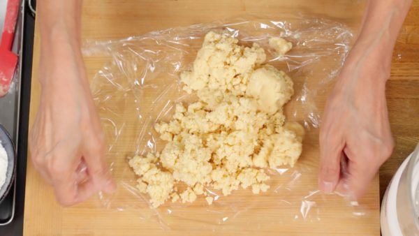 Place the mixture onto a work surface covered with a sheet of plastic wrap. Pull the edges of the plastic wrap to the center and gather the clumps into a ball. Then, flatten the dough.