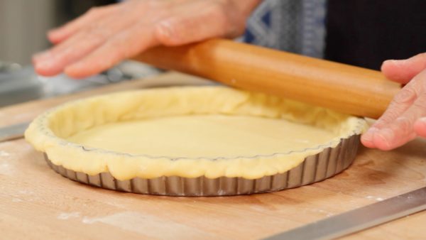 Cover the rim of the pan with the dough. Then, run the rolling pin along the top of the pan. Trim the edges of the dough to fit the tart pan. Lightly press the top and sides again to firmly attach them together.
