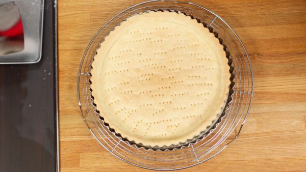 You will bake the crust with filling later so remove it when the whole surface is slightly browned. Place the pan onto a cooling rack. Let it sit to cool and then remove the tart crust from the pan.