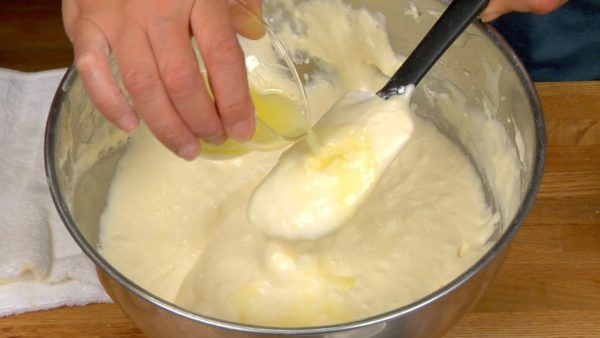 Quand toute la farine est mélangée, versez le mélange de beurre fondu sur la pâte. Brassez la pâte et laissez-la retomber doucement de la spatule. Recommencez cette opération environ 50 fois pour mélanger. 
