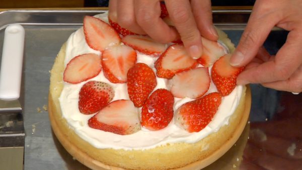 Mettez un peu de chantilly sur la moitié du gâteau du bas. Étalez la chantilly avec une spatule à glaçage. Couvrez la couche de crème avec des tranches de fraises. 