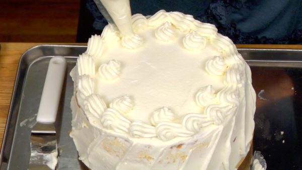 Formez des ronds avec la crème pour placer les fraises dessus ensuite. Placez la pointe de la spatule à glaçage entre le plateau tournant et le gâteau, tournez et grattez le surplus de crème.