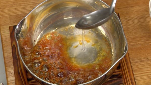 Rápidamente añade el agua caliente en 2 a 3 pasos con un cucharón de mango largo. Inclina la olla hacia afuera (no hacia donde estés tú) para prevenir que el caramelo caliente salte y te queme la mano. Mueve la olla para emparejar el caramelo caliente.