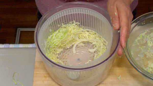 Let's prepare the side vegetables. Use a vegetable slicer and shred the cabbage into ice water. Let it sit in the water for 2 to 3 minutes. Drain the cabbage shreds with a salad spinner. Serve it on a plate. Garnish with the parsley, small tomamos and lemon wedges. Put the tartar sauce in a small cup and place it on the plate.