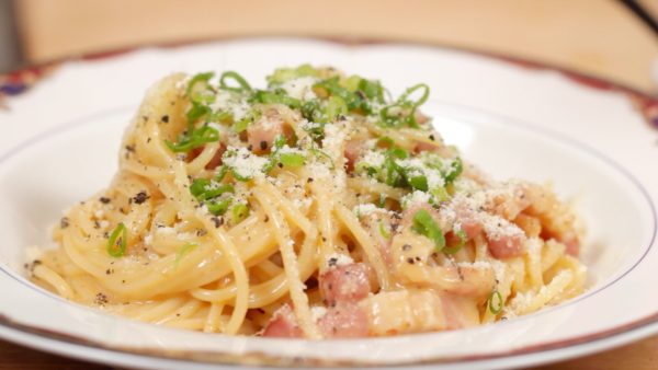Place the carbonara onto a plate. Top with the chopped spring onion leaves. Finally, sprinkle on the grated Parmesan cheese and black pepper.