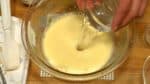 把鸡蛋糊再次搅打三分钟左右。鸡蛋糊的颜色会变成淡黄色，质地也会变得浓稠。将小苏打溶解在水中，再加入鸡蛋糊中搅打。