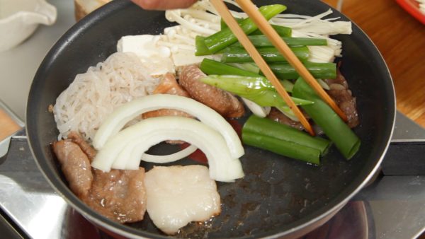 Place the beef on the edges of the pan. The caramelized sugar makes the additional ingredients more delicious. Add the yaki dofu, ito konnyaku, shiitake, enoki mushrooms, onion and spring onion leaves.