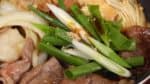Nous allons vous montrer comment ajouter des ingrédients au sukiyaki. Par exemple, ajoutez le vert des oignons nouveaux. Quand vous placez les nouveaux ingrédients dans le sukiyaki, ajoutez les assaisonnements. Saupoudrez de sucre. Et ajoutez la sauce soja. Mélangez les assaisonnements et le vert des oignons nouveaux est prêt. 