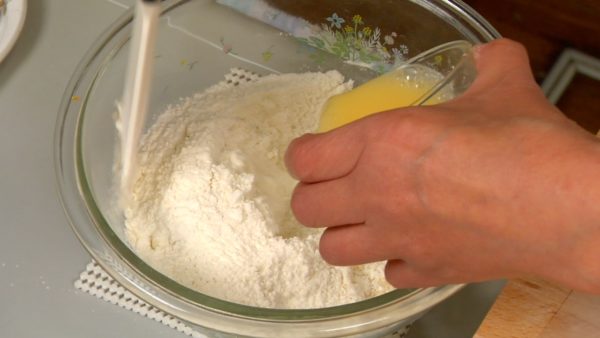 Let's make the bread dough next. Add the sugar, salt, non-fat dry milk powder and instant yeast to the bread flour. Whisk the flour mixture well. Dilute the beaten egg with the warm water. Gradually pour it into the flour and stir with a spatula until evenly mixed.
