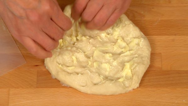 Flatten the dough and spread on the butter. Gather the rim of the dough toward the center and knead in the butter. When the butter is mixed in, gather the dough with the scraper and form a dough ball.