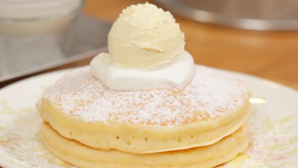 On a plate, place 2 pancakes on top of each other. Dust the pancakes with icing sugar. Place a dollop of whipped cream on top. And spoon the vanilla ice cream onto it.