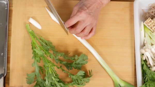 Let's prepare the ingredients. Slice the long green onion using diagonal cuts. As for the shungiku, use the soft upper half of the stalk and the bottom part of the leaves.