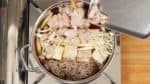 加入魔芋面条，烤过的豆腐（把它切成1.5厘米（0.6英寸））和长葱。再加入江之菇和姬菇。将鸡肉放入锅中。