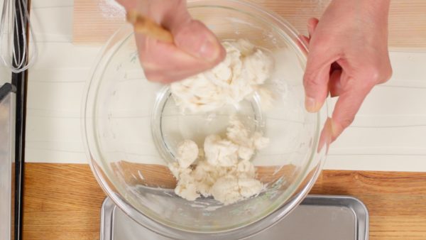 Ajoutez l'eau petit à petit pendant que vous mélangez avec des baguettes. Mélangez jusqu'à ce que toute la farine soit humidifiée. 