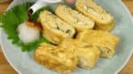 Das Tamagoyaki auf einem Teller anrichten. Geriebenen Daikon-Rettich leicht ausdrücken und daneben platzieren, etwas Sojasauce darüber gießen. Der geriebene Daikon ist sehr erfrischend zum Tamagoyaki.
