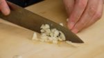 Cắt bỏ rẽ cuối của tép tỏi. Nghiền nát tỏi bằng cạnh dao. Sau đó, thái thô nó thành các miếng nhỏ hơn.