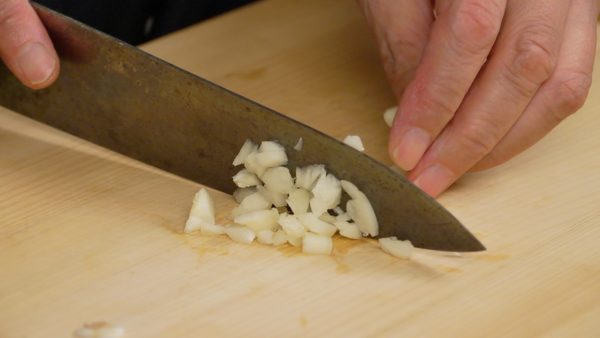 Retirez la partie racine de la gousse d'ail. Écrasez l'ail avec le côté du couteau. Ensuite, hachez-la grossièrement en petits morceaux. 