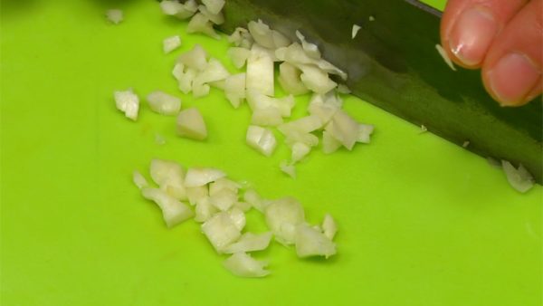 Schiacciate lo spicchio d'aglio con il lato piano del coltello. Spezzatelo a metà e rimuovete il germoglio all'interno. Sminuzzate l'aglio finemente.