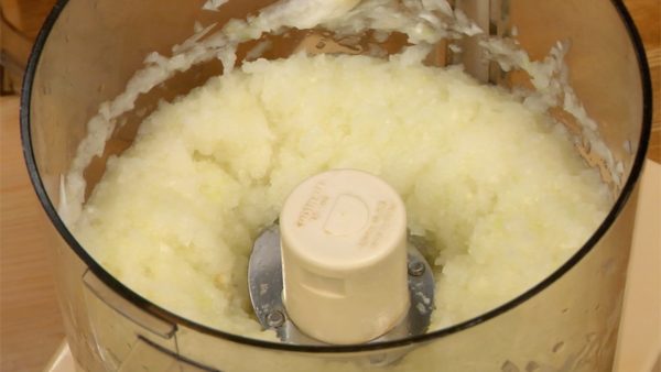 Let’s grate the onions using a food processor. Cut the onions in half and then into rough pieces. Put the pieces into the bowl and cover with a lid. Pulse several times and then turn on the processor. And now the onion is grated.