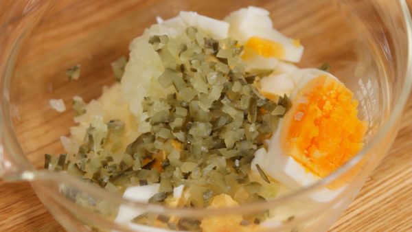 Using an egg slicer, cut half of the boiled egg into fine pieces. Add the egg to the mayonnaise. Add the chopped pickle to the mixture.