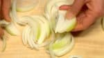 Vamos preparar os ingredientes para o Gyudon. Corte a cebola em fatias de 1 cm (0,4"). Separe as camadas com seus dedos. Rale o gengibre. Pique a cebolinha.