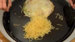 Tillsätt okonomiyakisåsen, fortsätt steka och rör om mycket, så att såsen fördelas jämnt under tiden. Forma nudlarna till en cirkel, och bryn ena sidan av dom.