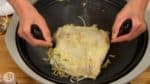 Levante o okonomiyaki com as espátulas e coloque-o sobre o macarrão.
