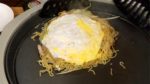 Setzt das Okonomiyaki mit der Nudelseite voran zügig auf das Ei und wendet es dann wieder auf die Teigseite.