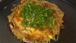 Coat the okonomiyaki with a generous amount of okonomiyaki sauce. Sprinkle on the bonito powder and the aonori seaweed. Finally, top with the chopped spring onion leaves and now it is ready to serve.