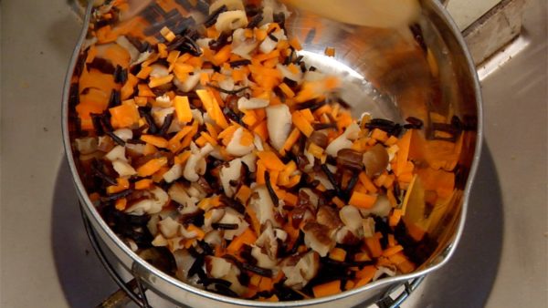 Let's stir-fry the ingredients. Heat the small pot on the burner. Heat the vegetable oil in the small pot. Put in the carrot, shiitake mushrooms and hijiki seaweed. Thoroughly stir-fry the ingredients.