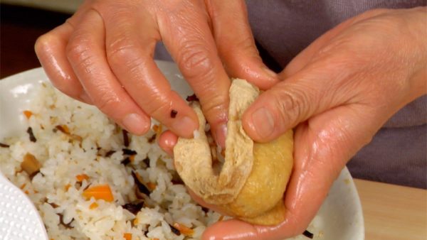 Nặn cơm dùng cho cơm cuộn thành một hình cầu nhỏ và nhồi nó vào mỗi túi đậu phụ. Điều chỉnh hình dạng và gấp chỗ hở của đậu phụ chiên. lặp lại quy trình này và làm 12 miếng Inarizushi.