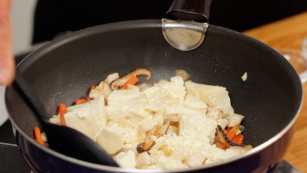 Now, the chicken is cooked. Remove the excess water from the tofu with a paper towel. Then, add the tofu. Roughly break the tofu into smaller pieces while sauteing.
