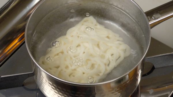 Let’s make the kitsune udon. Heat a bowl in a pot of hot water and remove. Place the frozen udon noodles into the boiling water.
