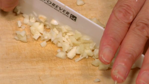Let's cut the vegetables. Remove the root end of the garlic clove. Crush the garlic clove with the flat side of a knife. Remove the skin and chop the garlic into fine pieces.