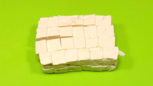 Nach 20 Minuten Entwässern den Tofu aus dem Papiertuch auswickeln, dabei vorsichtig sein, damit es nicht zerbricht. Den Tofu zuerst waagerecht in zwei Blöcke schneiden, dann senkrecht schneiden. Schließlich den Tofu in 1,5 cm-Würfel schneiden.