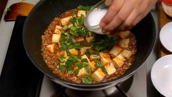 Add in the garlic chives and gently stir with the wooden spatula. Mix and dissolve the potato starch evenly before adding it to the Mapo Tofu. Lift the pan from the burner and pour in the potato starch while swirling the pan.