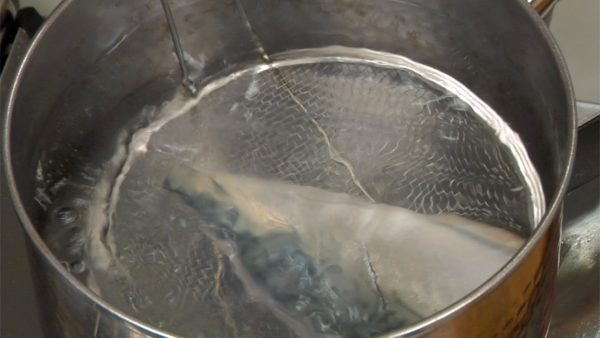 Add water to a large amount of boiling water to bring it just below the boiling point. With a mesh strainer, submerge a piece of mackerel into the hot water. When the surface turns white, immediately drop it into a bowl of ice water. Repeat this process for the other piece of mackerel.