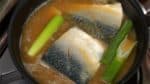 Drop in the ginger root slices and the green part of the long green onion. The onion will help cover the fishy smell.