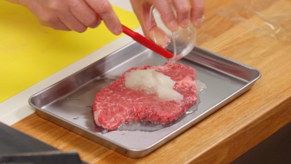 Verteilt die Hälfte des geriebenen Zwiebels auf ein kleines Blech und legt das Fleisch darauf. Dann bedeckt die obere Seite des Steaks mit dem restlichen Zwiebel. Die Enzyme des Zwiebels werden die Proteine des Fleisches aufspalten und das Fleisch extra zart machen. 