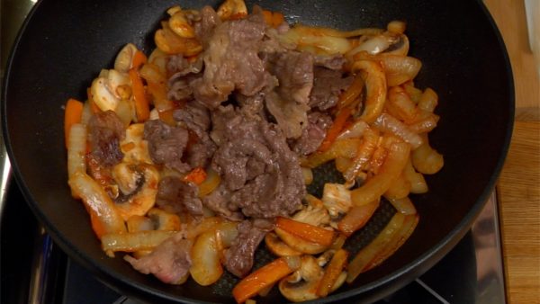 When the vegetables are well coated, place the beef slices back into the pan and distribute evenly among the vegetables. Add the red wine to the beef and vegetables and reduce the liquid on medium heat.