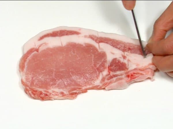 Let's prepare the pork loin slice. Make several cuts across the tough, stringy part between the fat and lean meat. Flip it over and repeat the process. This will prevent the pork slice from curling up when deep-fried.